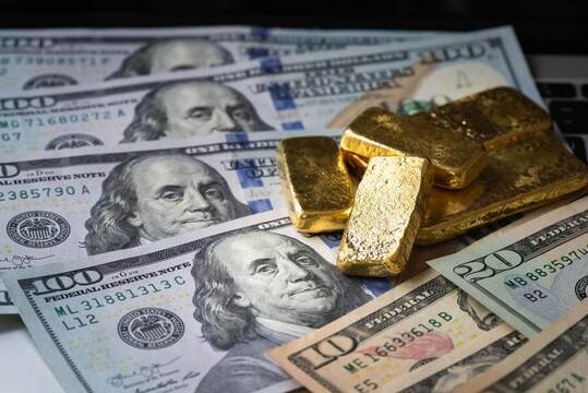 Impression monétaire record: qu’est-ce que ça signifie pour l'or? des billets de dollars avec des lingots d'or brut posés dessus symbolisant l'impression monétaire record qui est un facteur important pour le prix de l'or.