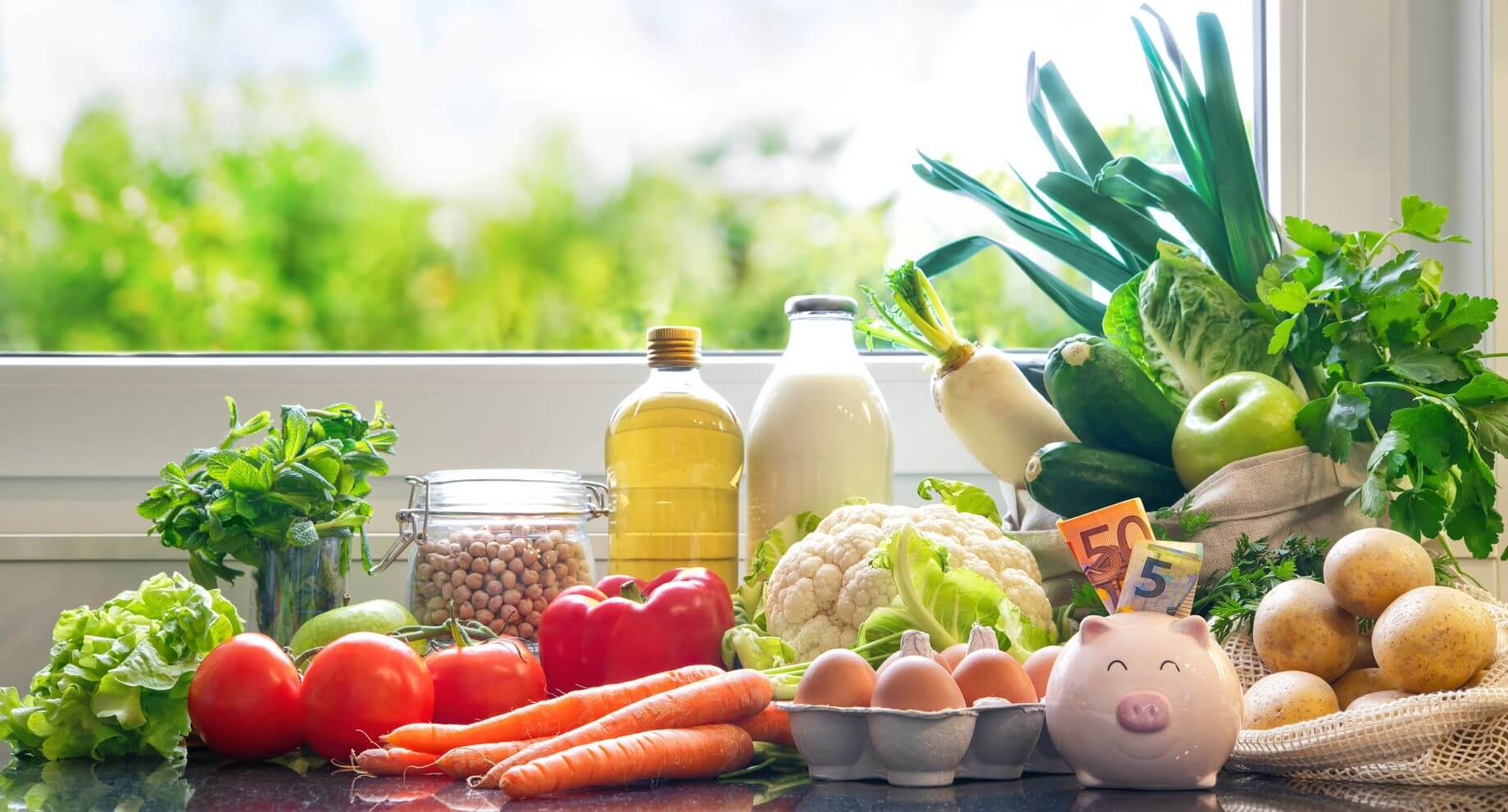 A photograph of various groceries near a piggy bank filled with 50 and 5 euro notes