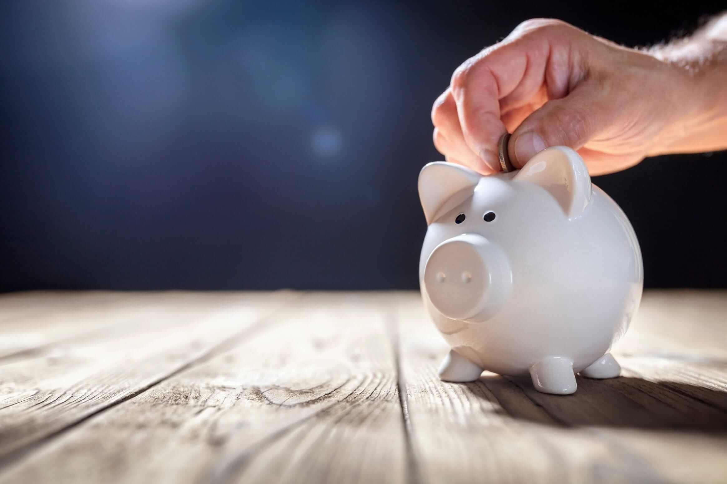 Eine Hand, die Geld in ein Sparschwein steckt