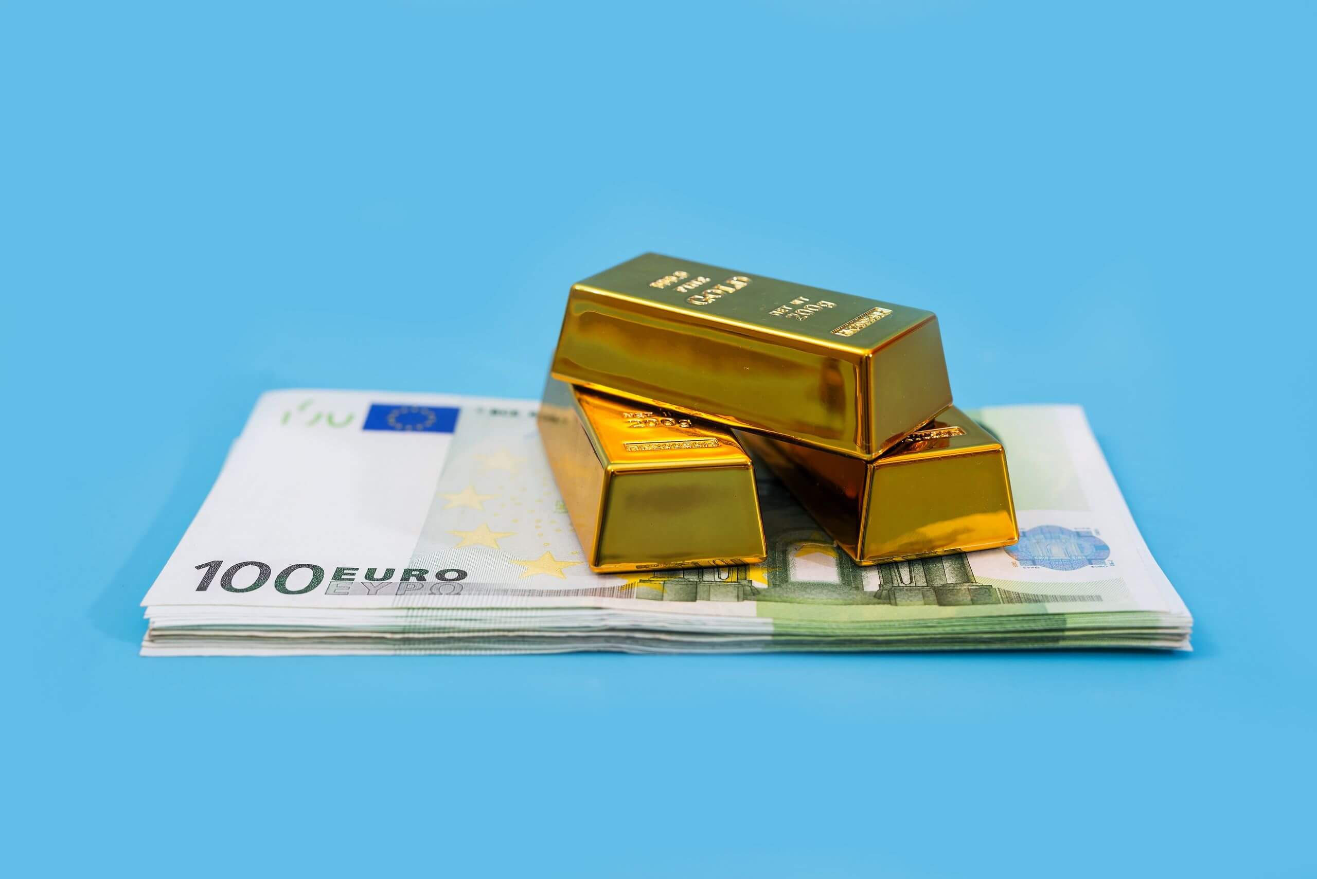 100 euro notes and three fine gold bars on top on a blue background