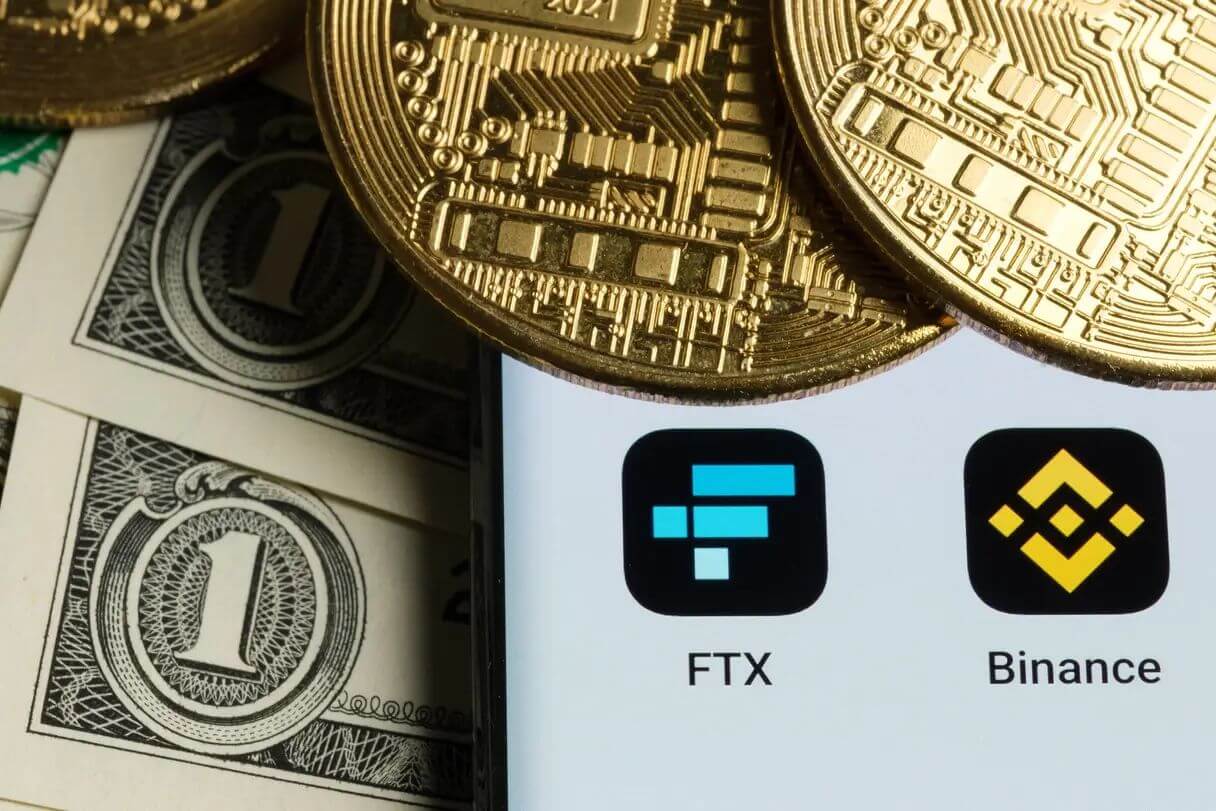 FTX and Binance apps in a phone put on dollar bills and gold bitcoin coins on it